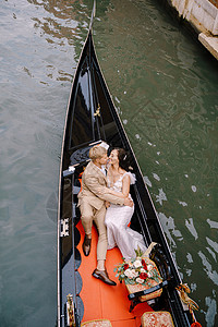 意大利威尼斯婚礼 一位船夫载着新娘和新郎乘坐经典的木制贡多拉沿着狭窄的威尼斯运河行驶 在古建筑的背景下 新婚夫妇坐在船上沙装丈夫图片
