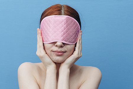 快乐的女士脸上戴着粉红色睡面具 在蓝色背景下图片