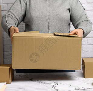 穿着灰色毛衣的女人拿着棕色纸箱白色开箱女性运输纸板盒子工作货物女士房间图片