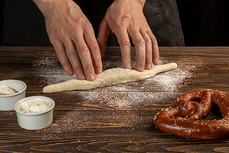 制作retzel的分步骤说明 厨师推出面团 并推出pretzel 黑暗背景糕点打样母猪食物酵母面粉木板碎肉深层厨房背景图片