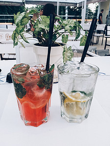 两杯冷柠檬水 加柠檬片 薄荷花瓣 冰块和草莓 夏季在咖啡厅的玻璃桌边图片
