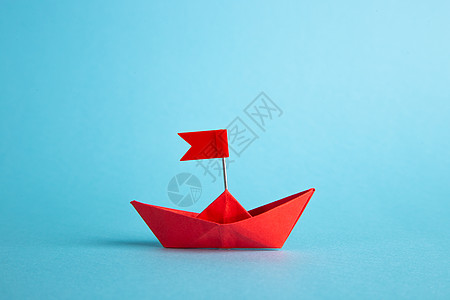 折纸背景红领头纸船在蓝背景上领先 领导理念 掌舵成功折纸优胜者钥匙竞赛领导者团队旅行监督船舶背景