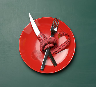 红色圆红板 叉子和刀 以绿色背景的绿色计量胶带包裹在绿色底盘上图片