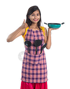 以白色背景持有厨房用的年轻印度妇女SPO STPULA 拖拉机和锅等围裙女孩女士勺子餐具烹饪金属衣服手势平底锅图片