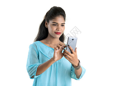 使用手机或白背景孤立的智能手机的年轻印度女孩 在白色背景下被隔离人士女性微笑空白视频屏幕商业细胞商务电话图片