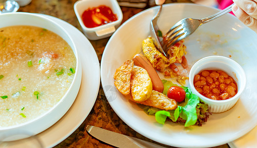 白稀饭人们在餐厅使用叉子和勺子吃早餐 白碗虾米粥或米粥 香肠和土豆片油炸 健康生活的早餐 健康食品背景