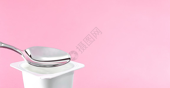粉红背景的酸果杯和银勺 含酸奶霜的白色塑料容器 用于健康饮食和营养平衡的新鲜奶制品饮食杯子小吃乳糖奶油牛奶生物食物勺子营养图片