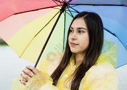 美丽的黑发美女 在雨中拿着多彩的雨伞快乐女士成人雨衣乐趣下雨彩虹街道喜悦天气图片