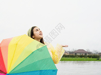 美丽的黑发美女 在雨中拿着多彩的雨伞乐趣喜悦雨衣快乐微笑幸福天气下雨女士彩虹图片