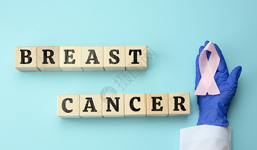 医生用蓝色手套的手握着粉色丝带 作为防治乳腺癌斗争的象征图片