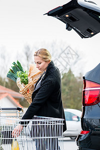 妇女购物后将杂货装进汽车后备箱杂货树干停车位加载篮子包装食物存储图片