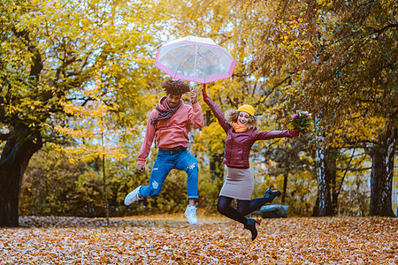 男人和女人在秋天公园快乐地跳跃丈夫下雨种族喜悦好心情妻子夫妻女士公园季节图片
