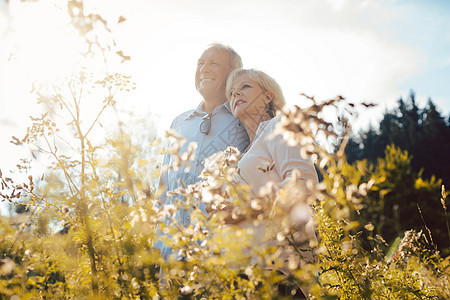 老夫妇在草地上肩并肩站立伙伴老年人阳光照射阳光男人夫妻退休微笑妻子风景图片
