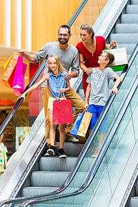 家庭在购物商场用自动扶梯带袋子的扶梯零售快乐母亲成人店铺顾客男人中心男生兄弟姐妹图片