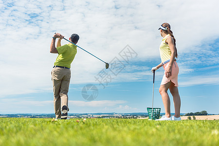 年轻女子在高尔夫课上练习正确运动高尔夫球微笑男性职业塑料女士晴天男人天空裙子图片