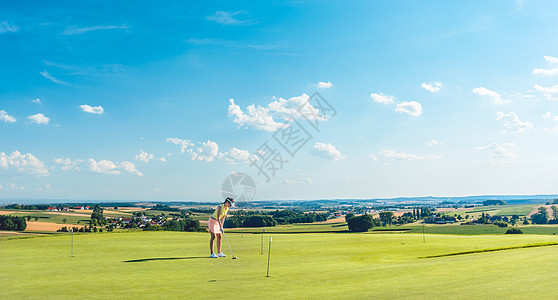 执着的年轻女子在训练区的草地上打高尔夫运动爱好土地娱乐推杆罢工天空中风女性练习背景图片