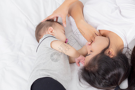 年轻的亚洲母亲抚摸着卧室床上柔软的小女婴的头 妈妈爱新生儿和照顾 与孩子一起表达的女人 父母和女儿 家庭观念女性婴儿新生女士母性图片