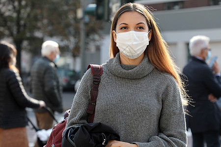 戴着外科口罩走在城市街道上的年轻女学生的画像 戴着口罩的女孩走在路上 尊重社会距离的人们在背景的红绿灯前停了下来图片