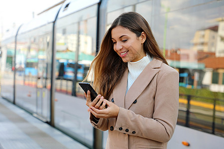 快乐的美丽女人在网页上持有关于城市交通的蜂窝更新信息 微笑的女商务人士对通过智能手机支付电动交通费用的在线票务服务感到满意图片