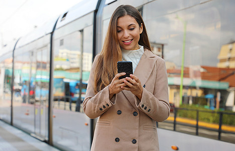 美丽的年轻女子拿着关于城市交通在线的蜂窝更新信息 微笑的女商务人士对通过智能手机支付电动交通费用的在线票务服务感到满意图片