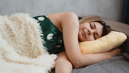 穿绿色睡衣的年轻美女 睡在黄色枕头上时间成人压痛乐趣微笑羽绒就寝女性沙发房间图片