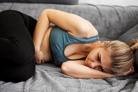 家庭沙发上躺着的胃痛妇女的侧面视线运动腹泻青少年套装女士腹部疼痛疾病腹痛女性图片