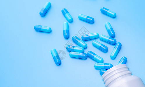蓝色胶囊药丸在蓝色背景下从瓶子里散开 医药行业 治疗新发传染病的药物开发和新药研究 胶囊丸业图片