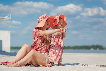 有个小女孩和她妈妈 在海滩沙滩上玩的漂亮晒太阳衣 时髦的家庭风貌 笑声情感快乐童年拥抱帽子幸福天空裙子婴儿海岸图片