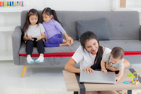 年轻的亚洲母亲在笔记本电脑上工作 同时在家照顾女儿 妈妈和女婴坐在一起使用笔记本视频通话 父母和亲密关系 室内 家庭和商业概念商图片