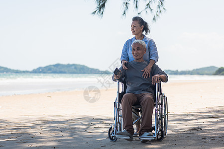 坐在轮椅上的高级男子和老年妇女 在沙滩上微笑的情侣图片