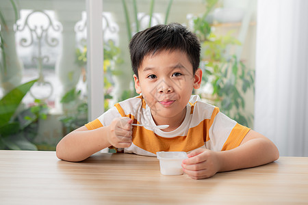 微笑的小男孩吃美味酸奶的肖像食物童年男生孩子小吃奶制品早餐营养勺子甜点图片