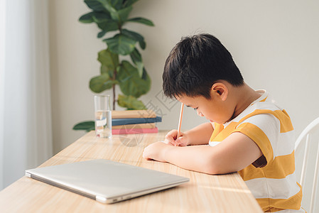 在校男孩在家庭坐椅上用笔记本电脑玩网上游戏互联网写作学习技术孩子男生学校桌子学生教育图片