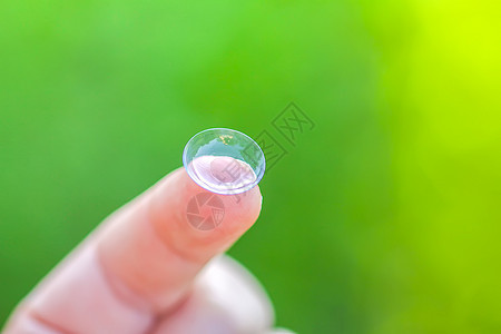 在绿色夏季自然背景模糊的指尖上用透明隐形透视镜矫正近视女性卫生验光师皮肤白色角膜镜片光学图片