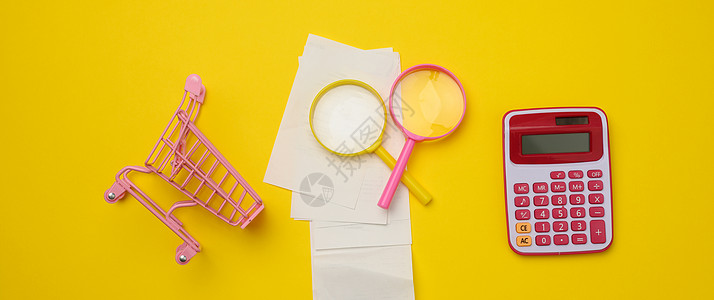一堆纸检查一个粉红色的塑料计算器和一个黄色背景上的放大镜 家庭预算审计概念图片