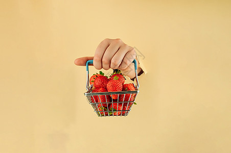 女孩手里拿着一个购物篮 里面装着成熟的红草莓 女人的手在撕破的纸上 网上购物的概念美食购物饮食农业水果销售大车零售购物车甜点图片