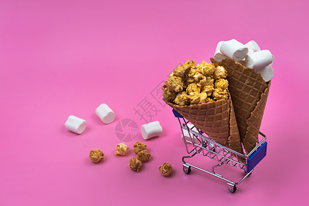 有冰淇淋甜食和粉红背景糖果的购物车大车爆米花杂货店小吃购物食物粉红色消费者贸易店铺图片