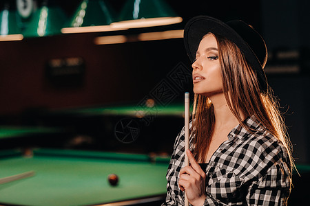 一个戴着帽子的女孩 在台球俱乐部 手里握着一个提示闲暇枕头衬衫水池台球奢华台球桌绿盖桌子娱乐图片