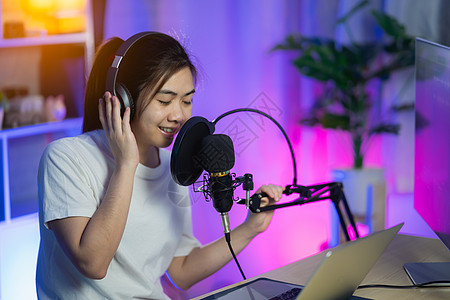 女歌手在家庭录音室用耳机唱着新歌的女歌手记录麦克风电脑女士笔记本说话艺人音乐女性明星图片