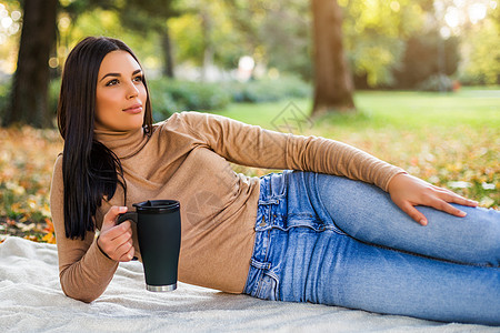 妇女在秋季在公园享受喝咖啡的同时饮用咖啡毛衣杯子愿望太阳毯子休闲活动喜悦女性晴天图片