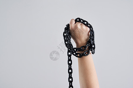 女性拳头握着金属链 在灰色背景上高举铁链图片