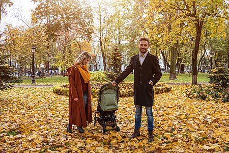 在秋天的公园里散步 年轻的家庭带着婴儿车里的新生婴儿 在金色的秋天公园户外的家庭 着色图像可爱的高清图片素材