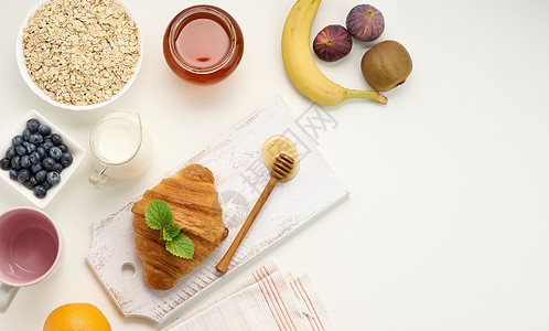 早餐早饭 陶瓷板上生燕麦片 脱甘油牛奶 蓝莓和白桌上的罐子蜂蜜勺子杯子橙子稀饭营养奇异果粮食薄荷饮食桌子图片