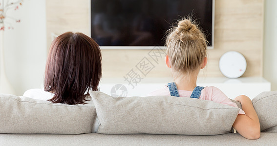 母亲和女儿坐在沙发上 看电视 家庭时间概念 背视图片