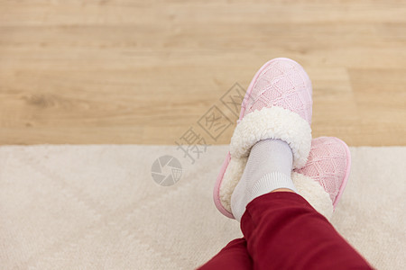 穿着粉红色编织拖鞋的交叉腿粉色卧室鞋类女孩女士羊毛地面裤子红色白色图片