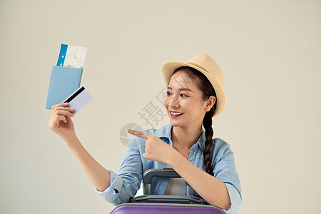 美丽的亚洲年轻女性戴着帽子 上面显示信用卡和护照 并指着暑假旅行 度假的女孩用卡支付金融图片