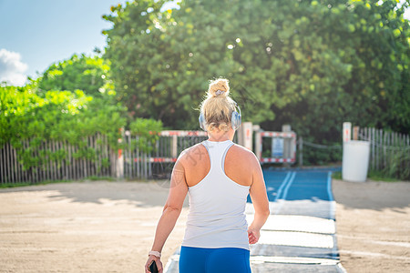 迈阿密夏日海滩上穿着运动服 带无线入耳式耳机的健身女性听音乐赛跑者小路跑步运动装玩家女士运动慢跑者身体训练图片