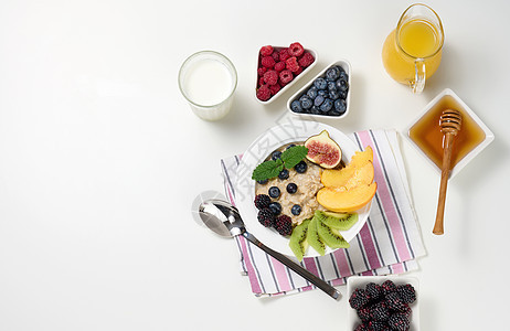 牛奶 燕麦粥和水果盘 透明玻璃瓶中的鲜榨果汁 白色桌子上碗中的蜂蜜 健康早餐制品勺子稀饭粮食谷物食物甜点水果小吃盘子图片