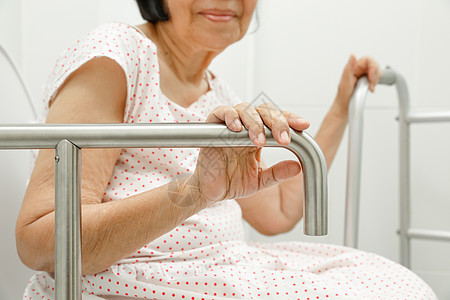 手机上的医院老年妇女在厕所的手扶机上安全洗手间医院酒吧栏杆皱纹女士机动性医学祖母背景