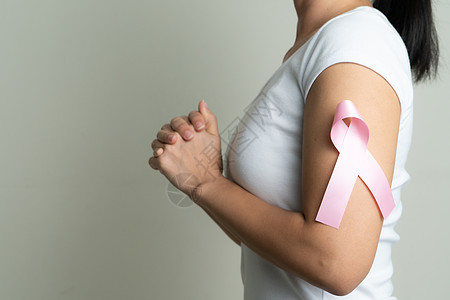 在祈祷女性手臂支持乳腺癌病因的粉红色徽章丝带上 乳癌意识概念图片