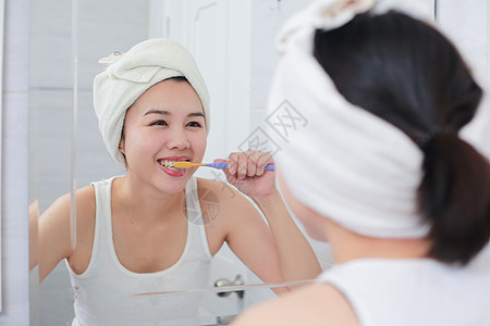 年轻的亚洲女人在镜子前刷牙图片